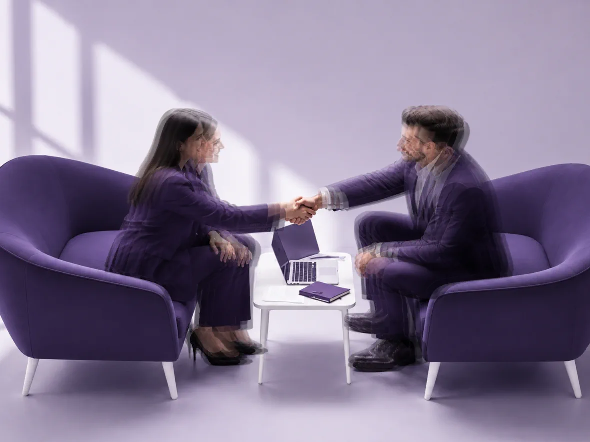 Two people meeting across a low table with a laptop open between them.